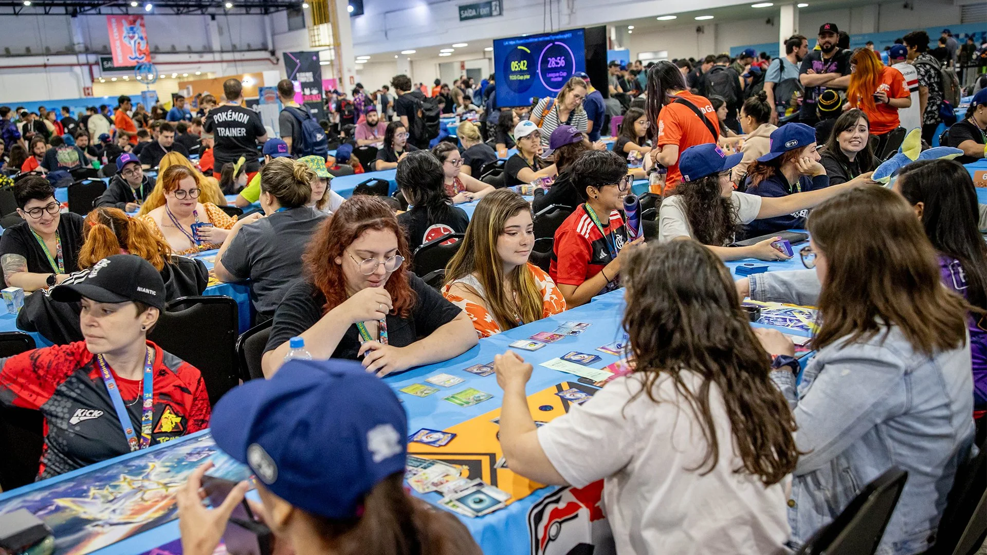 Asistentes jugando y conversando alrededor de mesas de cartas coleccionables en una convención.